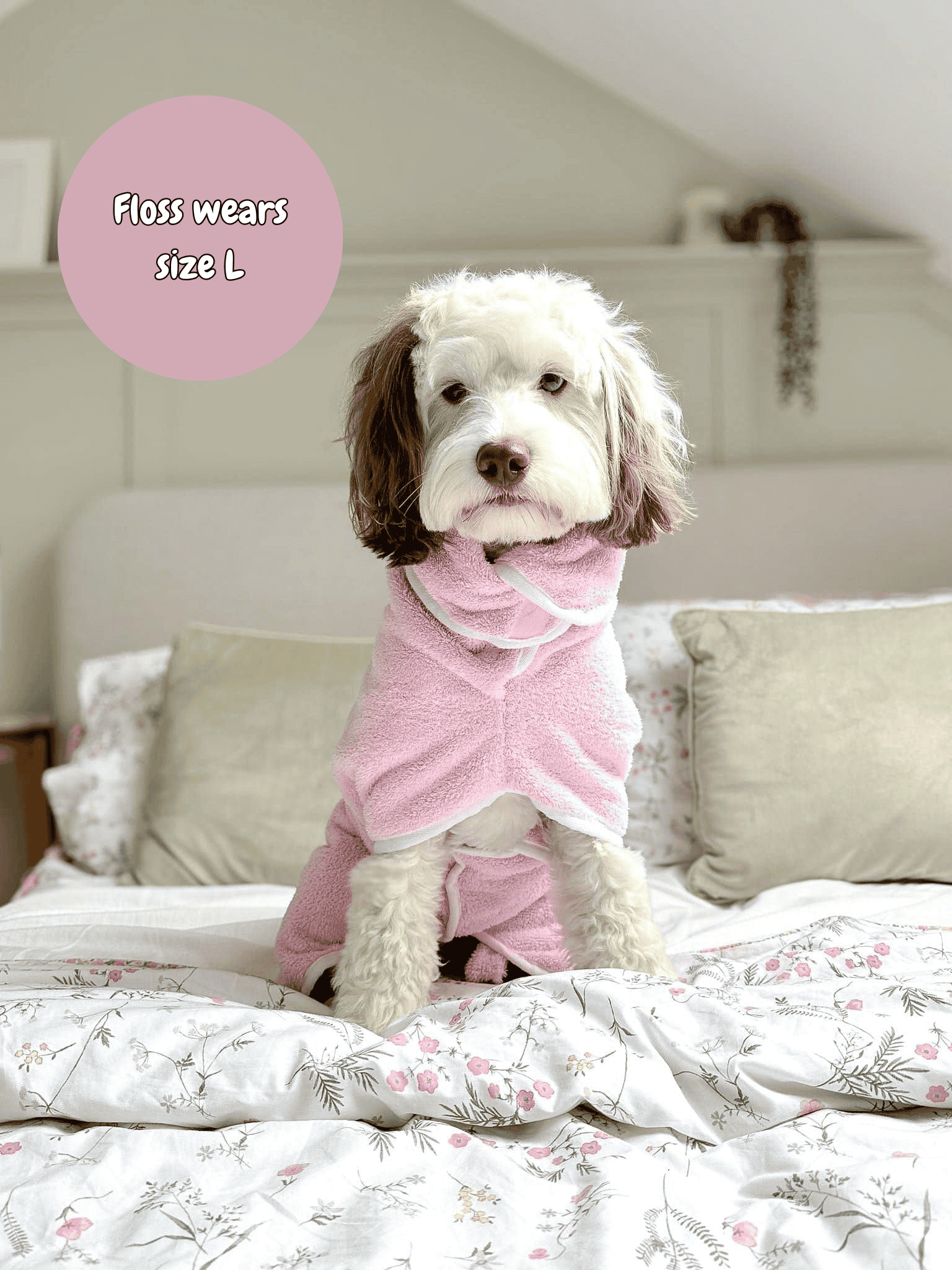 Dog wearing a pink robe on a bed with a pink label indicating size L.
