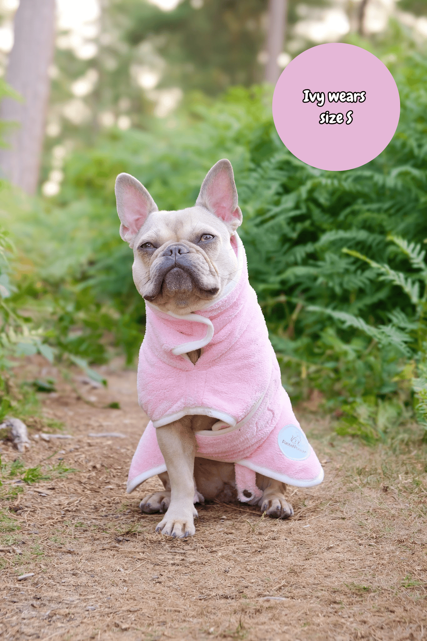 Dog wearing a pink robe with text indicating size on a natural background