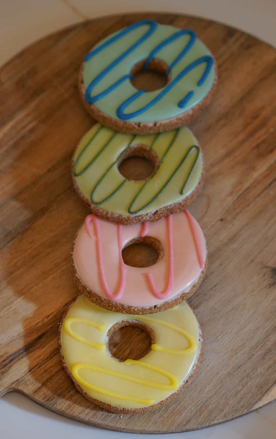 Four colorful donut-shaped cookies on a wooden board