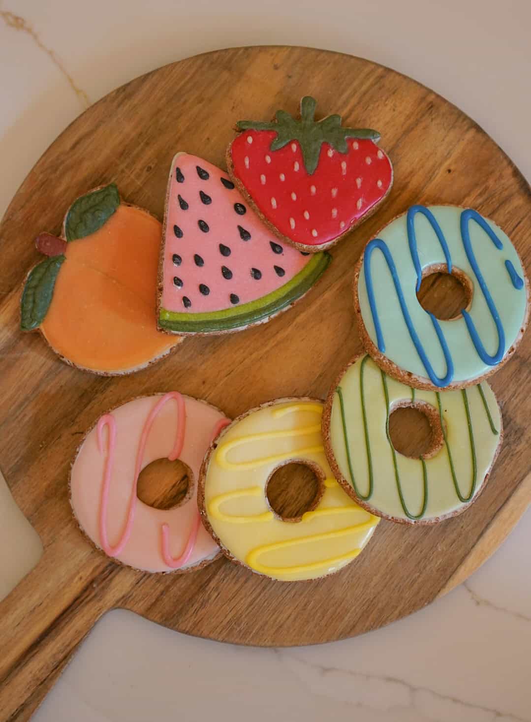 Wooden board with colorful cookies shaped like fruits and donuts.