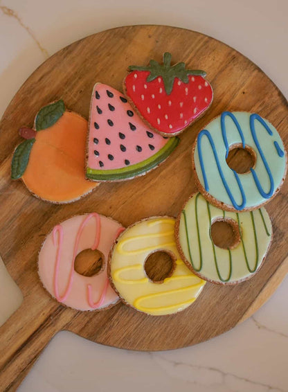 Wooden board with colorful cookies shaped like fruits and donuts.