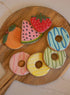 Wooden board with colorful cookies shaped like fruits and donuts.